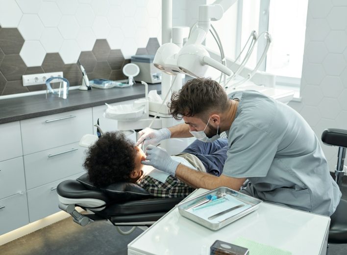 Contemporary dentist bending over little patient Contemporary dentist bending over little patient